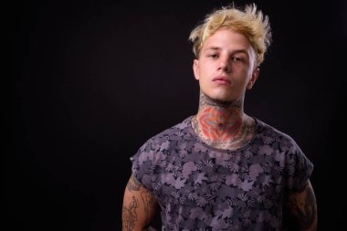 Studio shot of young handsome rebellious man with blond hair and tattoos against black background