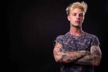 Studio shot of young handsome rebellious man with blond hair and tattoos against black background