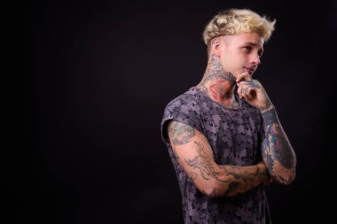 Studio shot of young handsome rebellious man with blond hair and tattoos against black background