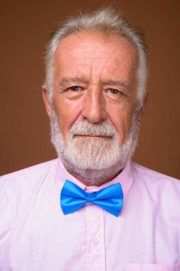 Studio shot of senior handsome man wearing stylish clothes against brown background