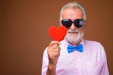 Studio shot of senior handsome man wearing stylish clothes against brown background