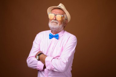 Studio shot of senior handsome tourist man wearing stylish clothes against brown background