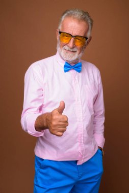 Studio shot of senior handsome man wearing stylish clothes against brown background