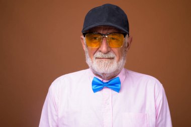 Studio shot of senior handsome man wearing stylish clothes against brown background