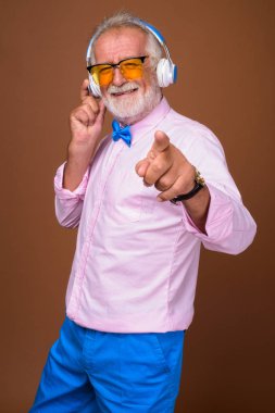Studio shot of senior handsome man wearing stylish clothes against brown background
