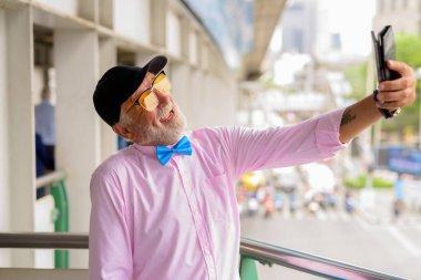 Portrait of handsome senior tourist man wearing stylish clothes while exploring the city of Bangkok, Thailand