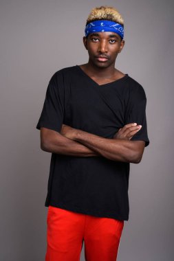 Studio shot of young African man wearing blue bandanna as headband against gray background