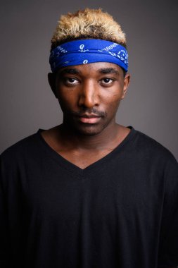 Studio shot of young African man wearing blue bandanna as headband against gray background
