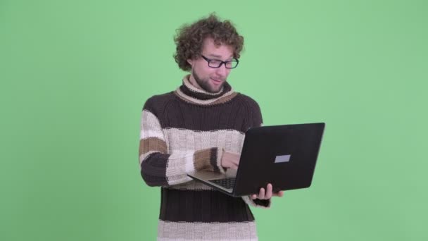 Feliz joven barbudo pensando mientras se utiliza el ordenador portátil — Vídeos de Stock