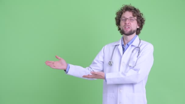 Счастливый молодой бородатый врач показывает что-то и получает хорошие новости — стоковое видео