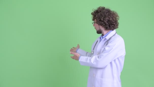 Stressed young bearded man doctor showing something to the back and giving thumbs down — Stock Video