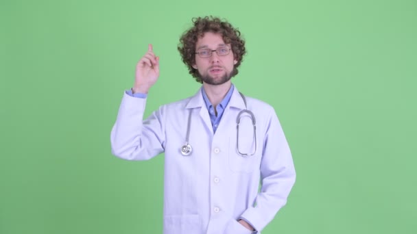 Happy young bearded man doctor talking while pointing up — Stock Video