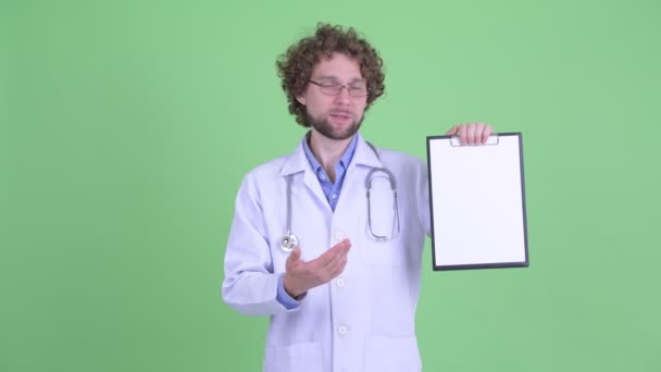 Benadrukte jonge bebaarde man arts presenteren met Klembord en het geven van duimen naar beneden — Stockvideo