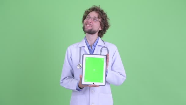 Glücklicher junger bärtiger Mann Arzt denkt, während er digitales Tablet zeigt — Stockvideo