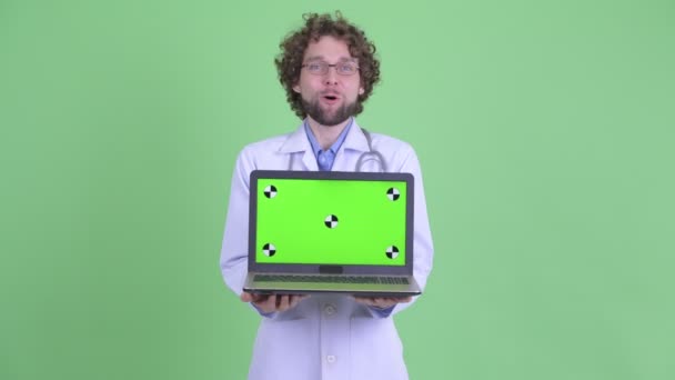 Gelukkige jonge bebaarde man arts die laptop toont en op zoek verrast — Stockvideo