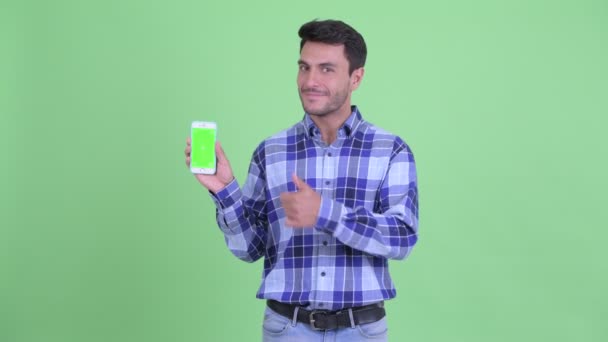 Щасливий молодий Іспанець людина показує телефон і даючи великі пальці вгору — стокове відео