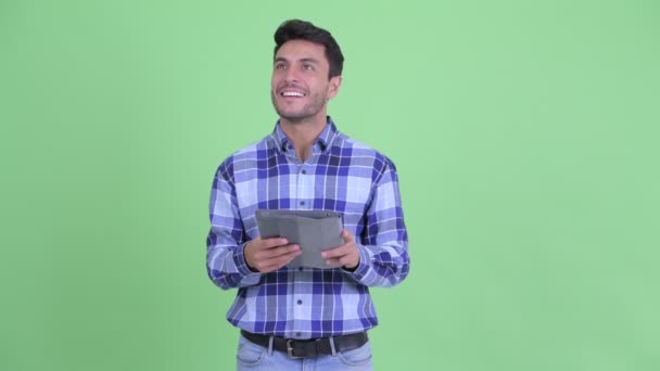 Jovem feliz homem hispânico pensando ao usar tablet digital — Vídeo de Stock