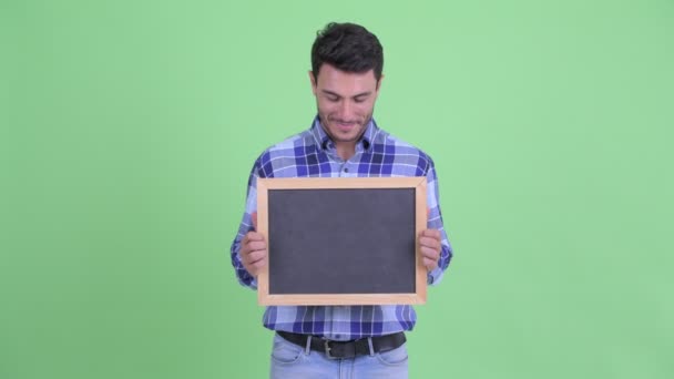 Feliz jovem hispânico homem pensando enquanto segurando quadro negro — Vídeo de Stock