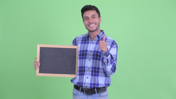 Jovem hispânico feliz segurando quadro negro e dando polegares para cima — Vídeo de Stock