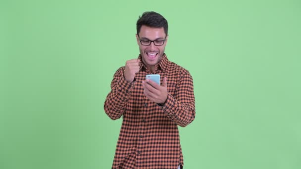 Feliz joven hipster hispano usando el teléfono y recibiendo buenas noticias — Vídeos de Stock