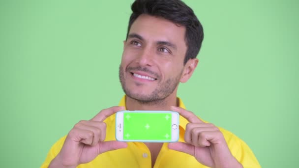 Gesicht eines glücklichen jungen hispanischen Geschäftsmannes, der beim Vorzeigen seines Telefons denkt — Stockvideo