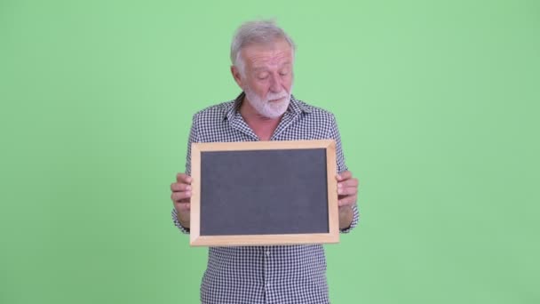 Mutlu üst düzey sakallı adam kara tahta tutan ve şaşırmış görünümlü — Stok video