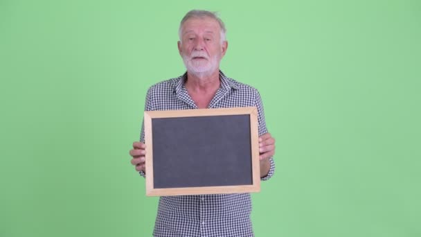 Homem barbudo sênior feliz falando enquanto segurando quadro negro — Vídeo de Stock