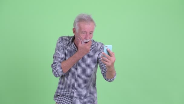 Στρεσαρισμένος γέρος με γένια χρησιμοποιώντας το τηλέφωνο και φαίνεται σοκαρισμένος — Αρχείο Βίντεο