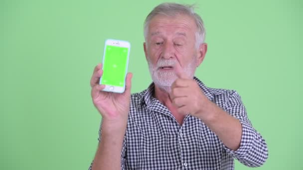 幸せな先輩ひげの男の顔は、携帯電話を示し、親指を与える — ストック動画