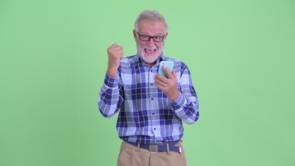 Homem hipster barbudo sênior feliz usando telefone e recebendo boas notícias — Vídeo de Stock