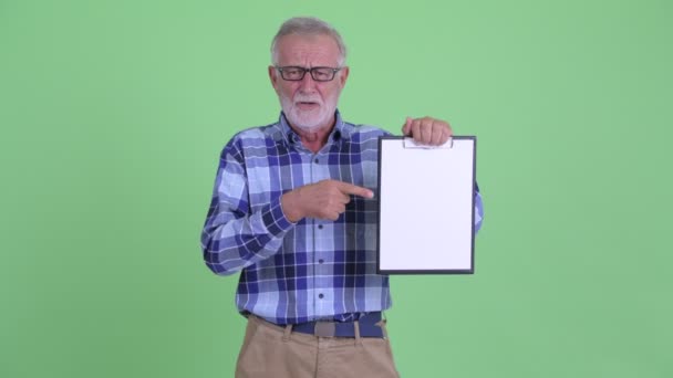 Stresset, eldre, skjeggete hipstermann som viser skriveplate og gir tomler ned – stockvideo