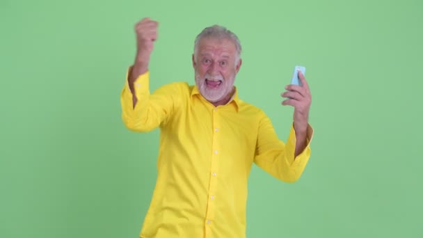 Feliz hombre de negocios barbudo mayor recibiendo buenas noticias y mostrando el teléfono — Vídeos de Stock