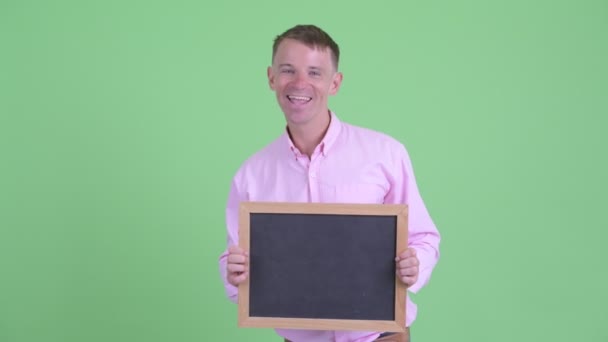 Retrato de hombre de negocios feliz sosteniendo pizarra y mirando emocionado — Vídeos de Stock