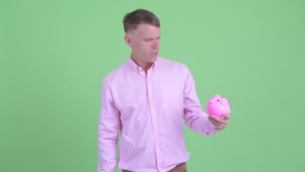Gestresster Geschäftsmann hält Sparschwein und drückt Daumen — Stockvideo