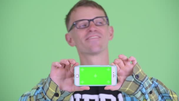 Gesicht eines glücklichen Nerd-Mannes, der beim Vorzeigen seines Telefons denkt — Stockvideo