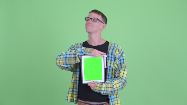 Porträt eines glücklichen Nerd-Mannes, der beim Vorzeigen eines digitalen Tablets denkt — Stockvideo