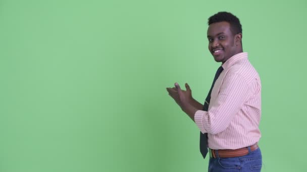 Szczęśliwy młody afrykański biznesmen pokazując coś na plecach — Wideo stockowe