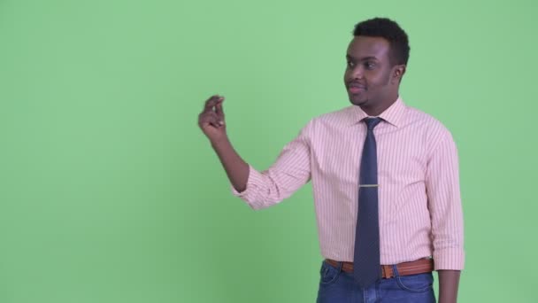 Ευτυχισμένος νεαρός Αφρικανός επιχειρηματίας που δαγκώνει τα δάχτυλα και δείχνει κάτι — Αρχείο Βίντεο