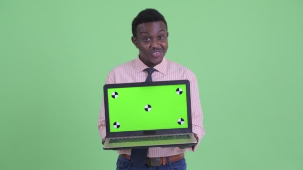 Счастливый молодой африканский бизнесмен показывает ноутбук и выглядит удивленным — стоковое видео