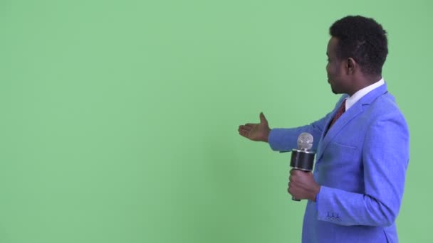 ニュースキャスターとして幸せな若いアフリカのビジネスマンは、何かを提示 — ストック動画