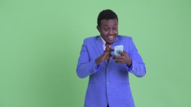 Mutlu genç Afrikalı işadamı telefon kullanarak ve şaşırmış görünümlü