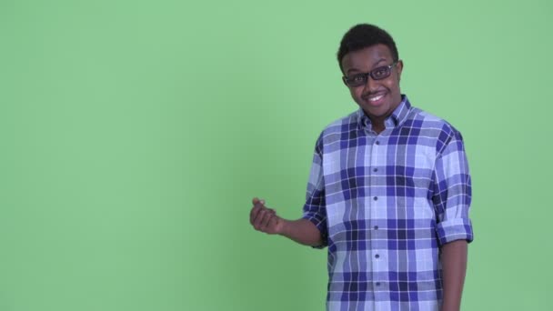 Glücklicher junger afrikanischer Hipster, der mit den Fingern schnippt und etwas zeigt — Stockvideo