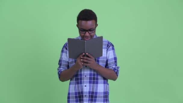 Shy young African hipster man covering face with book — Stock Video