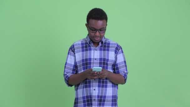 Lycklig ung afrikansk hipster man tänkande när du använder telefonen — Stockvideo