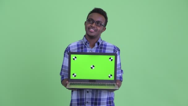 Happy young African hipster man thinking while showing laptop — Stock Video