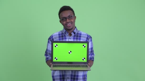 Happy young African hipster man talking while showing laptop — Stock Video