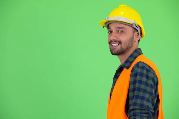 Perfil vista de feliz jovem barbudo homem persa trabalhador da construção sorrindo e olhando para a câmera — Fotografia de Stock