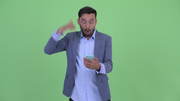 幸せな若いひげのペルシャのビジネスマンは、携帯電話を使用して、良いニュースを取得 — ストック動画