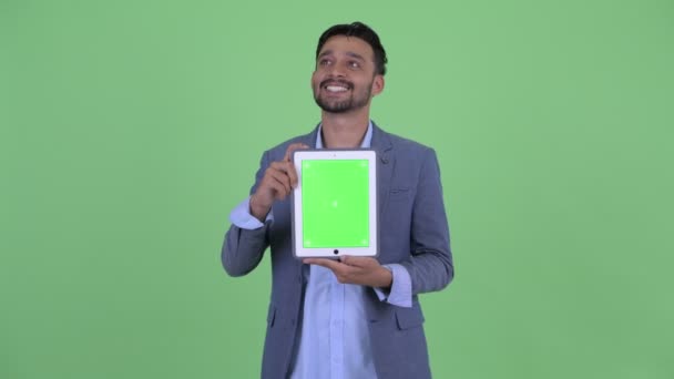 Счастливый молодой бородатый персидский бизнесмен думает, показывая цифровой планшет — стоковое видео