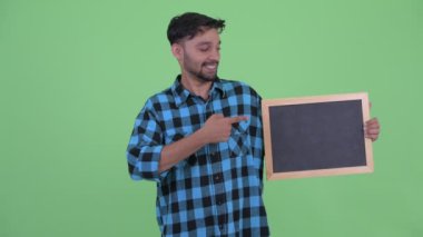 Mutlu genç sakallı Farsça hipster adam kara tahta tutan ve başparmak veren